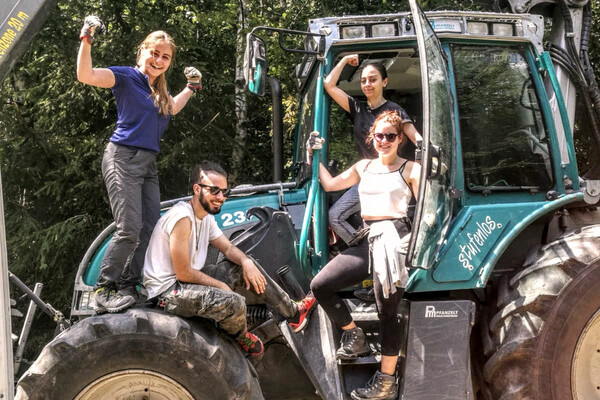 Vier Freiwillige stehen und sitzen auf einem Traktor und lächeln in die Kamera.