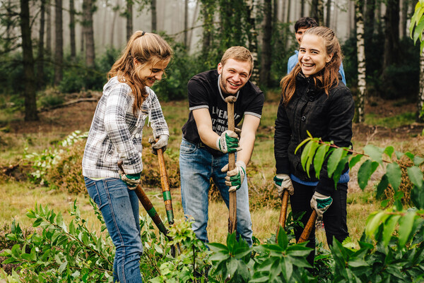 Drei Freiwillige in der Natur mit Gartengeräten, lächeln in die Kamera.
