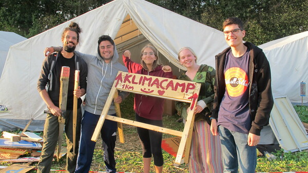 Fünf Freiwillige halten ein Holdzschild mit Aufschrift: 1km bis Klimacamp