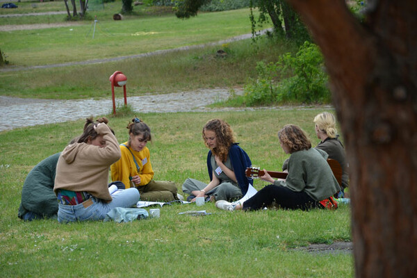 Sechs Personen sitzen auf einer Wiese und singen zum Gitarrenspiel